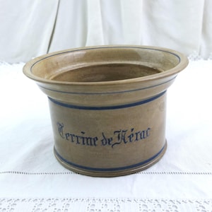 Può includere: Una terrina in ceramica beige con dettagli blu e la scritta "Terrine de Hérac". La terrina ha un'ampia apertura e un corpo cilindrico. Fasce blu circondano la parte superiore e inferiore.