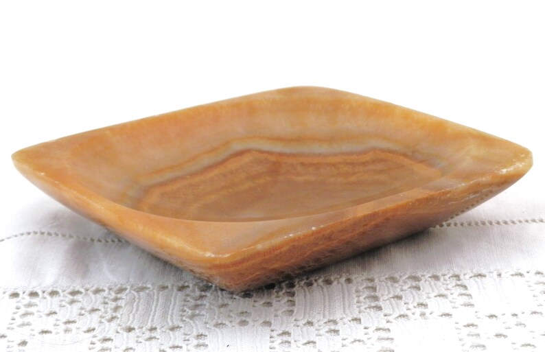 May include: A square, light brown, onyx dish with a slightly raised rim. The dish has a natural, striated pattern.