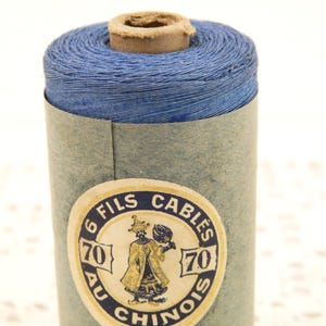 May include: A spool of blue thread with a label that reads "6 Fils Cables 70 Au Chinois 70".