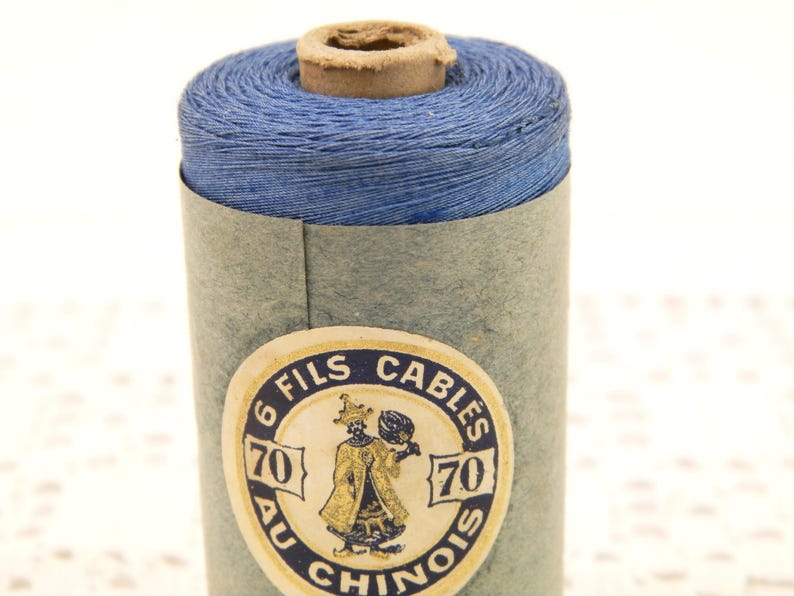 May include: A spool of blue thread with a label that reads "6 Fils Cables 70 Au Chinois 70".