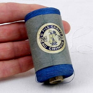 May include: A spool of blue thread with a label that reads "6 Fils Cables 70 Au Chinois 70".