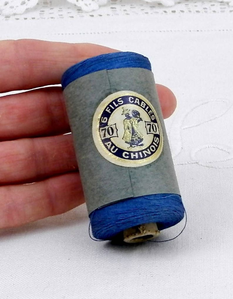 May include: A spool of blue thread with a label that reads "6 Fils Cables 70 Au Chinois 70".