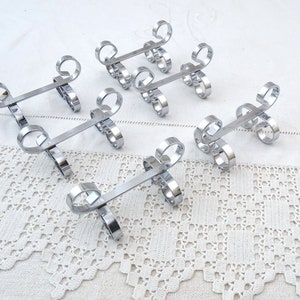 May include: Set of six silver-toned metal napkin rings with a decorative swirl design. Each ring is about 3 inches long.
