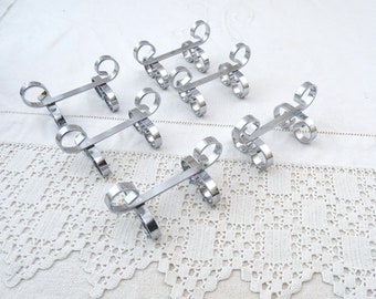 May include: Set of six silver-toned metal napkin rings with a decorative swirl design. Each ring is about 3 inches long.