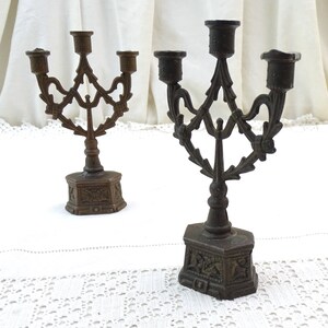 May include: Two antique bronze candle holders with ornate designs. Each holder has three candle arms and a decorative base.