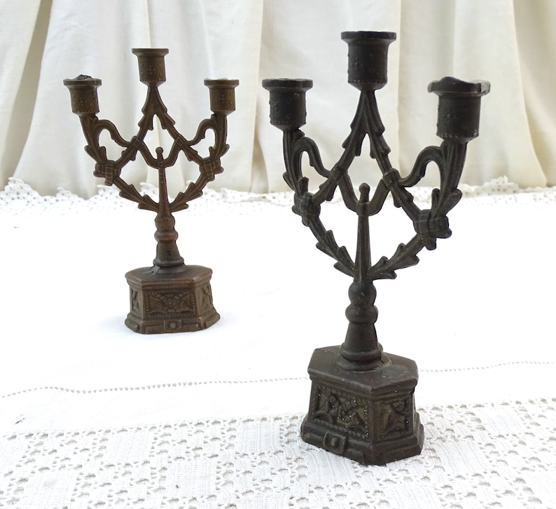May include: Two antique bronze candle holders with ornate designs. Each holder has three candle arms and a decorative base.