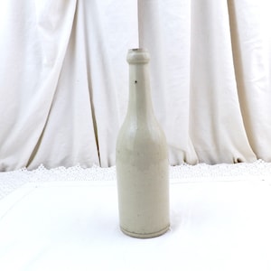 May include: A vintage ceramic bottle with a light gray glaze. The bottle has a rounded body and a narrow neck.