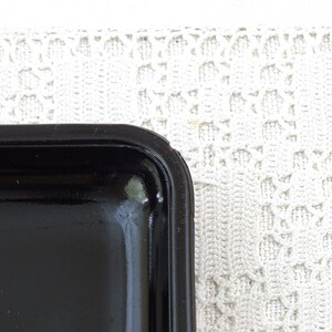 May include: A black rectangular tray with a raised edge. The tray has a glossy finish and is decorated with a colorful illustration of a person in a red and yellow costume.