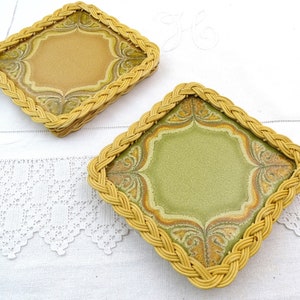 Puede incluir: Dos posavasos cuadrados de cerámica con un marco de mimbre tejido. Los posavasos tienen un diseño floral marrón y verde.