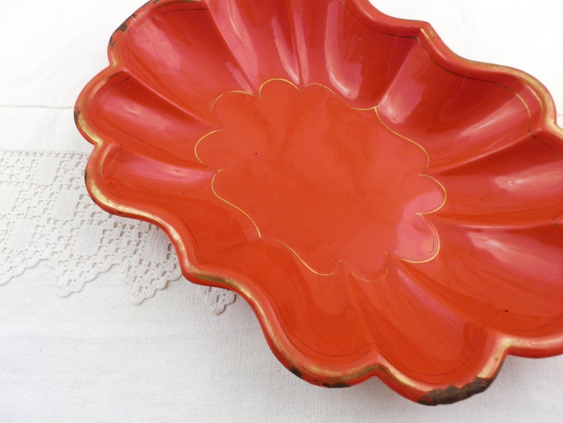 May include: A bright orange, scalloped serving dish with a gold rim and a gold design in the centre.