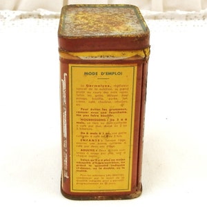 Puede incluir: Una lata rectangular vintage con una apariencia oxidada y envejecida. La lata es principalmente roja con una etiqueta amarilla con texto en franc&eacute;s, incluyendo "MODE D'EMPLOI". La parte superior de la lata es de un color m&aacute;s oscuro, parduzco.