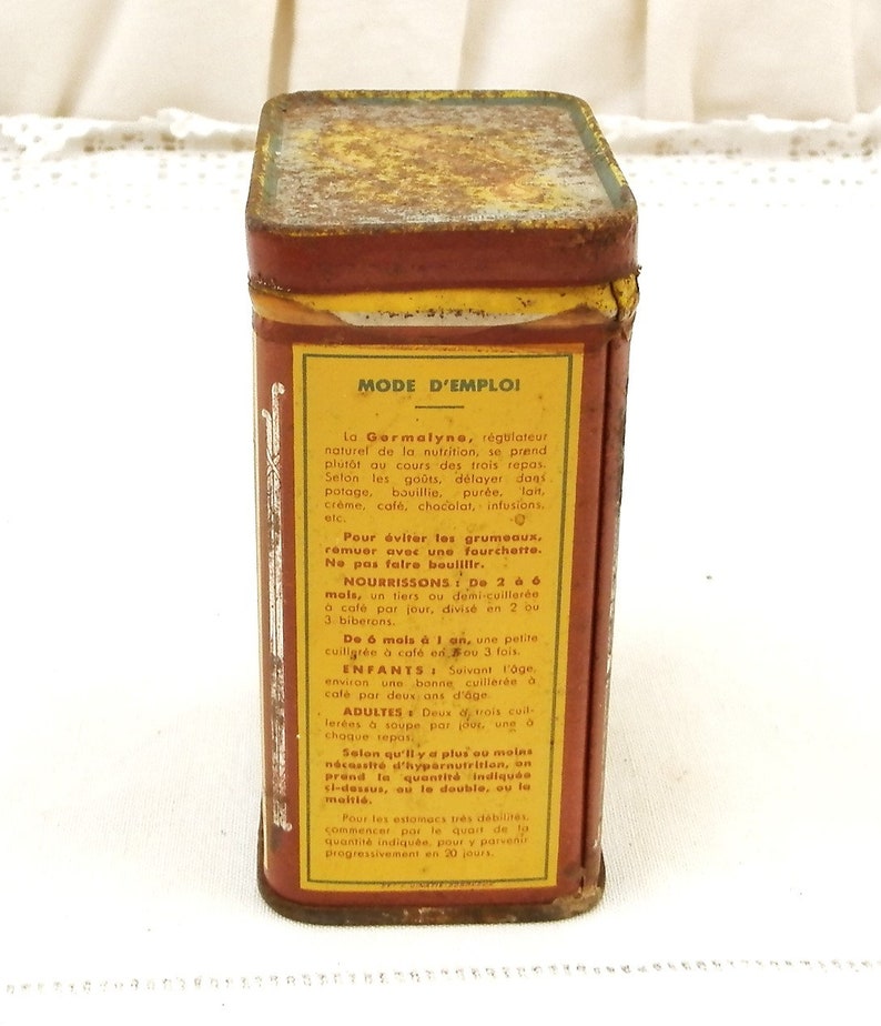 Puede incluir: Una lata rectangular vintage con una apariencia oxidada y envejecida. La lata es principalmente roja con una etiqueta amarilla con texto en franc&eacute;s, incluyendo "MODE D'EMPLOI". La parte superior de la lata es de un color m&aacute;s oscuro, parduzco.
