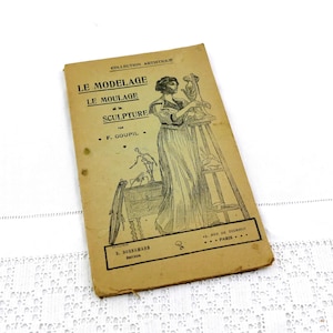 May include: Vintage book cover with the title "LE MODELAGE LE MOULAGE et la SCULPTURE" in black text. The cover features an illustration of a woman sculpting, with additional text and a decorative border. The book has a worn, aged appearance.