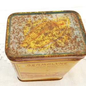 Puede incluir: Una lata rectangular antigua, con una combinaci&oacute;n de colores amarillo y marr&oacute;n. La tapa presenta una ilustraci&oacute;n y texto descoloridos. La palabra "GERMALYNE" es visible en el lateral. La lata muestra signos de desgaste, con &oacute;xido y decoloraci&oacute;n.
