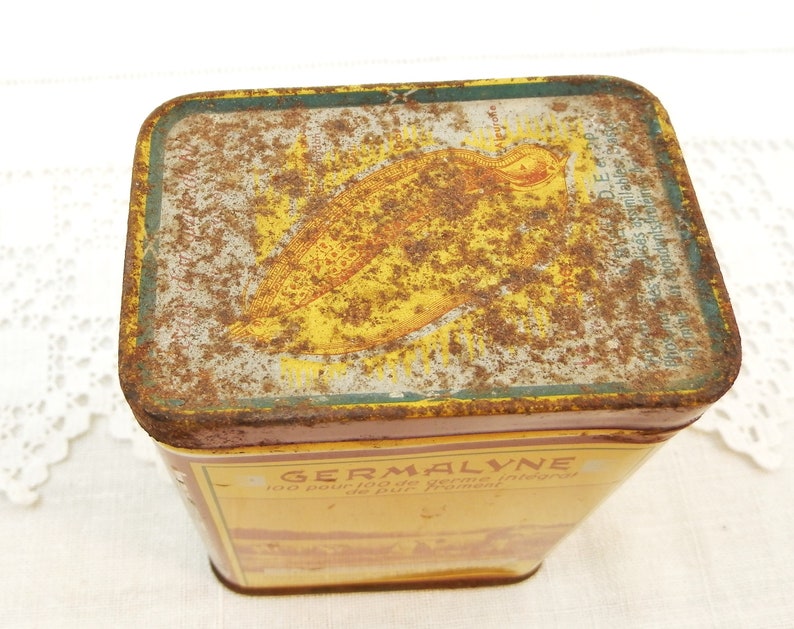 Puede incluir: Una lata rectangular antigua, con una combinaci&oacute;n de colores amarillo y marr&oacute;n. La tapa presenta una ilustraci&oacute;n y texto descoloridos. La palabra "GERMALYNE" es visible en el lateral. La lata muestra signos de desgaste, con &oacute;xido y decoloraci&oacute;n.