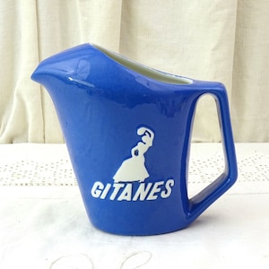 May include: A blue ceramic pitcher with a white silhouette of a woman and the word "Gitanes" in white lettering.