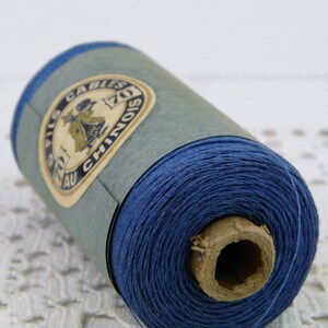 May include: A spool of blue thread with a label that reads "FILS AU CHINOIS 70Z CABLES".