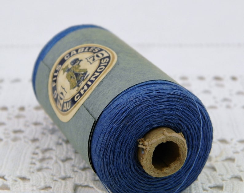May include: A spool of blue thread with a label that reads "FILS AU CHINOIS 70Z CABLES".