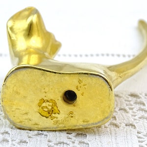 May include: Gold-toned metal cat figurine with a long, curved tail. The figurine is sitting on a white surface. The bottom of the figurine has a small hole.