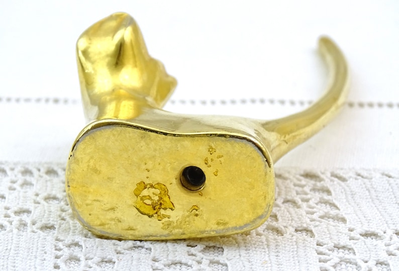May include: Gold-toned metal cat figurine with a long, curved tail. The figurine is sitting on a white surface. The bottom of the figurine has a small hole.