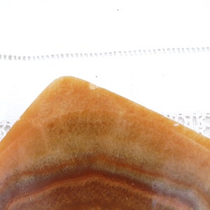 May include: A square, shallow dish made of brown and white alabaster with a striated pattern. The dish is empty and has a smooth, polished surface.