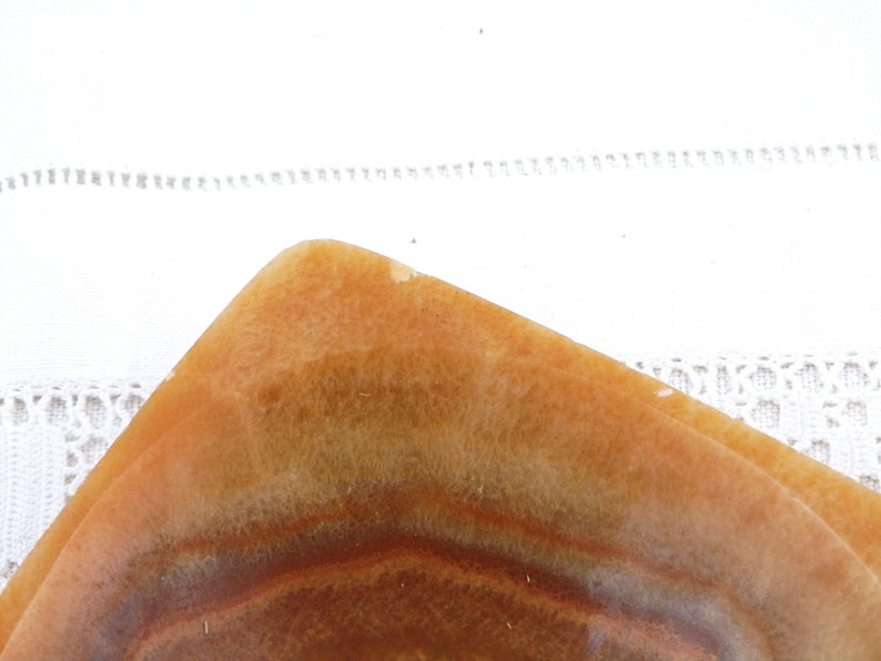 May include: A square, shallow dish made of brown and white alabaster with a striated pattern. The dish is empty and has a smooth, polished surface.