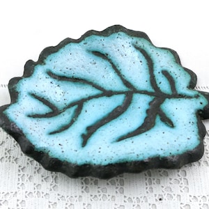 May include: A leaf-shaped ceramic dish with a light blue interior and dark brown edges and veins. The dish is on a white lace surface. Decorative and functional, it can be used as a trinket tray or a small serving dish.