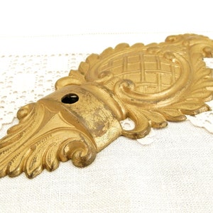 May include: A gold-toned metal decorative ornament with a detailed floral design and a woven pattern in the center. The ornament has a hole in the center, suggesting it may be a wall mount or a part of a larger piece.