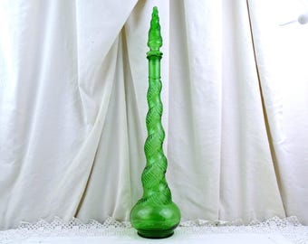 May include: A tall, green glass bottle with a spiral design and a pointed stopper. The bottle has a bulbous base and a long, twisted neck. The stopper is also green and has a textured, pointed top. The bottle is displayed against a white background.