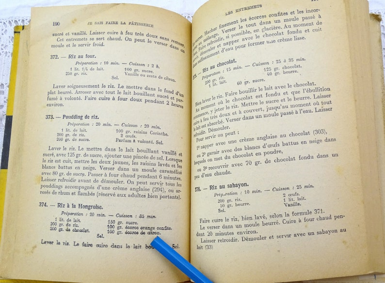 Pode incluir: Um livro de cozinha franc&ecirc;s vintage aberto em uma p&aacute;gina com instru&ccedil;&otilde;es para fazer arroz com leite. A p&aacute;gina est&aacute; amarelada pelo tempo e tem notas escritas &agrave; m&atilde;o com tinta azul.