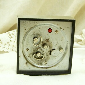 Puede incluir: Un reloj despertador vintage plateado con una esfera negra y un bot&oacute;n rojo. El reloj tiene una inscripci&oacute;n manuscrita en la parte posterior que dice "HPM 122214".