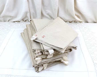 May include: A stack of 10 off-white linen tea towels with red embroidered numbers and a white tag on each towel.