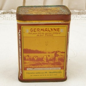 Puede incluir: Una lata rectangular de Germalyne con una etiqueta amarilla y marr&oacute;n. La etiqueta presenta texto y una ilustraci&oacute;n de personas cosechando trigo. La lata tiene una apariencia oxidada y envejecida, lo que sugiere que es vintage.