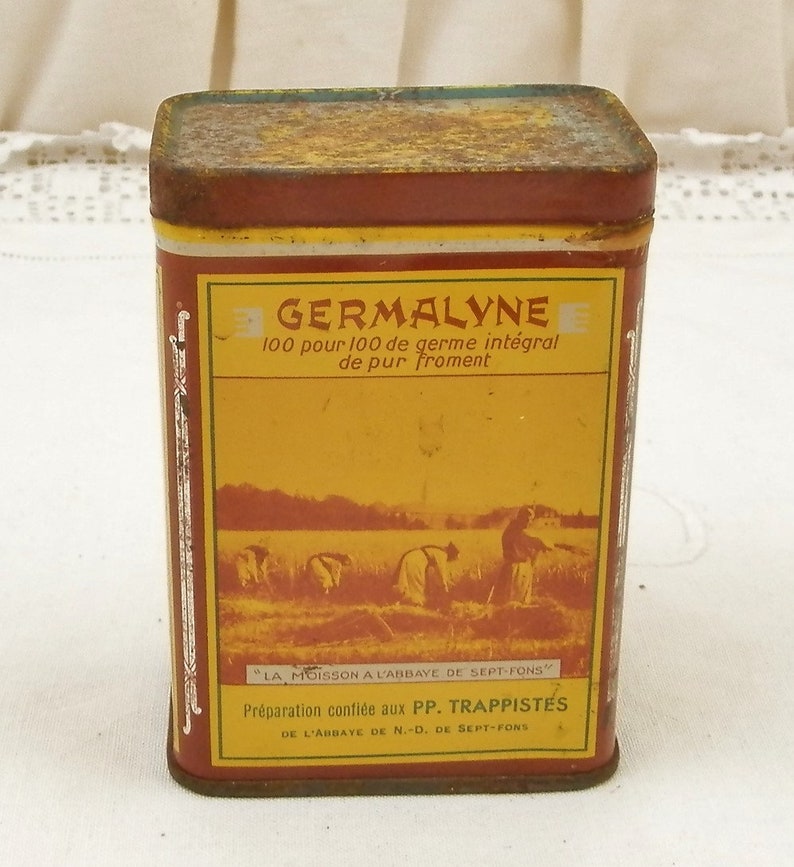 Puede incluir: Una lata rectangular de Germalyne con una etiqueta amarilla y marr&oacute;n. La etiqueta presenta texto y una ilustraci&oacute;n de personas cosechando trigo. La lata tiene una apariencia oxidada y envejecida, lo que sugiere que es vintage.