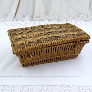 Op de afbeelding: Een rechthoekige, geweven rieten mand met een scharnierend deksel. De mand heeft een warme, lichtbruine kleur en een gestructureerd oppervlak. Het deksel en de zijkanten hebben een geribbeld ontwerp. De mand wordt waarschijnlijk gebruikt voor opslag of weergave.