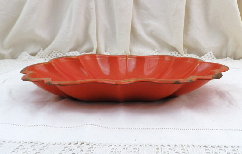 May include: A large, orange, scalloped serving bowl with a gold rim. The bowl is made of metal and has a shiny finish.