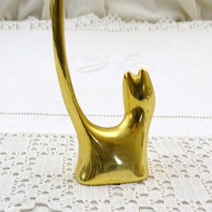 May include: Gold-colored metal ring holder shaped like a cat. The cat is sitting with its tail curled up in the air.