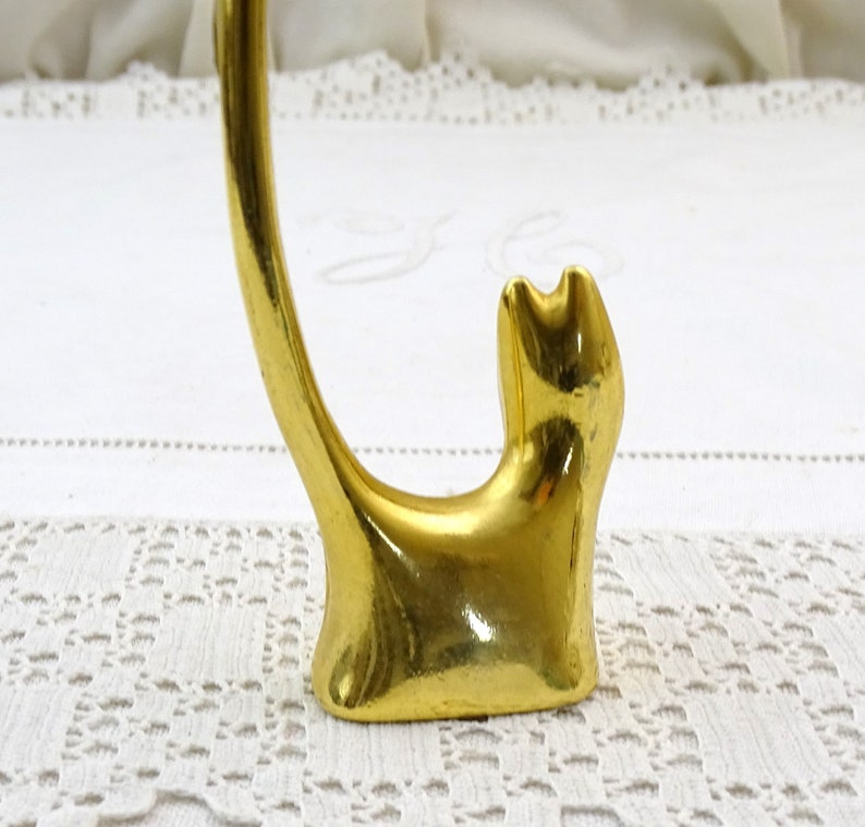 May include: Gold-colored metal ring holder shaped like a cat. The cat is sitting with its tail curled up in the air.