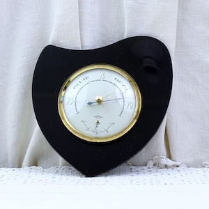May include: A black heart-shaped barometer with a gold-rimmed face. The face has a needle pointing to the "Pluie" and "Beau" markings.