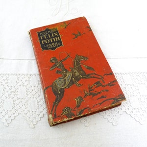 May include: Vintage red agenda book with gold lettering and illustrations. The cover features a knight on horseback with a bow and arrow, and the text "AGENDA FELIX POTIN 1924". The book is slightly worn, with visible signs of age.