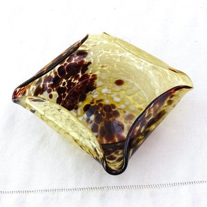 May include: A square-shaped glass bowl with a mottled brown and yellow pattern. The bowl has a wavy edge and is made of clear glass with brown and white flecks.