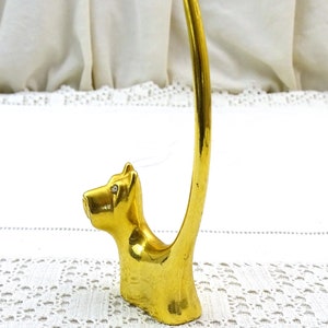 May include: Gold-toned ring holder shaped like a Scottish terrier dog with rhinestone eyes. The dog's tail is curled up to form a ring holder.