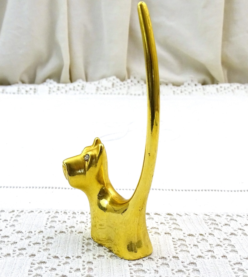 May include: Gold-toned ring holder shaped like a Scottish terrier dog with rhinestone eyes. The dog's tail is curled up to form a ring holder.