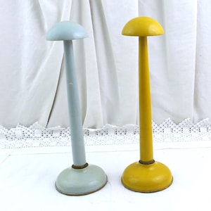 May include: Two vintage hat stands. One is light blue, the other is yellow. Each stand has a round base, a long, slender stem, and a rounded top. The stands are made of painted metal and are displayed against a white background.