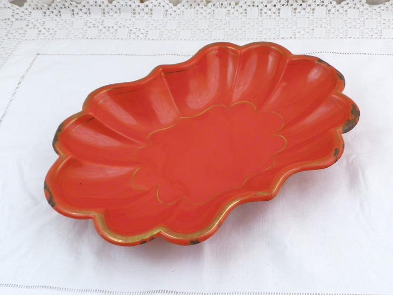 May include: An orange oval-shaped serving dish with a scalloped edge and gold trim. The dish is made of metal and has a shiny finish.