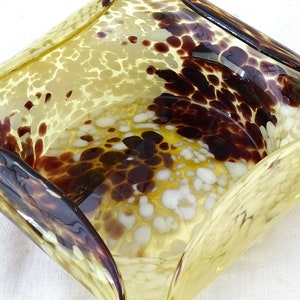 May include: A yellow glass bowl with brown and white speckled pattern. The bowl has a wavy, organic shape.