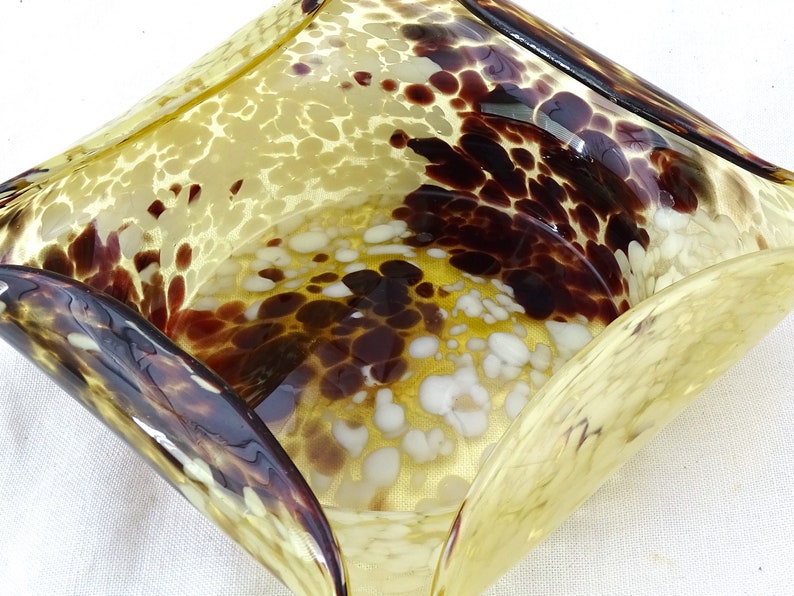 May include: A yellow glass bowl with brown and white speckled pattern. The bowl has a wavy, organic shape.