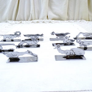 May include: Set of ten silver-toned metal animal napkin holders. Each holder features a different animal design, including a duck, a goose, a chicken, a lion, and an elephant.