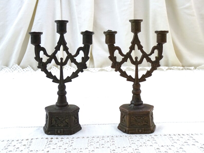 May include: Two antique bronze candle holders with a decorative, ornate design. Each holder has three candle arms and a hexagonal base.