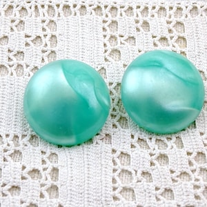 May include: A pair of round, turquoise blue, iridescent earrings. The earrings have a smooth, shiny finish.